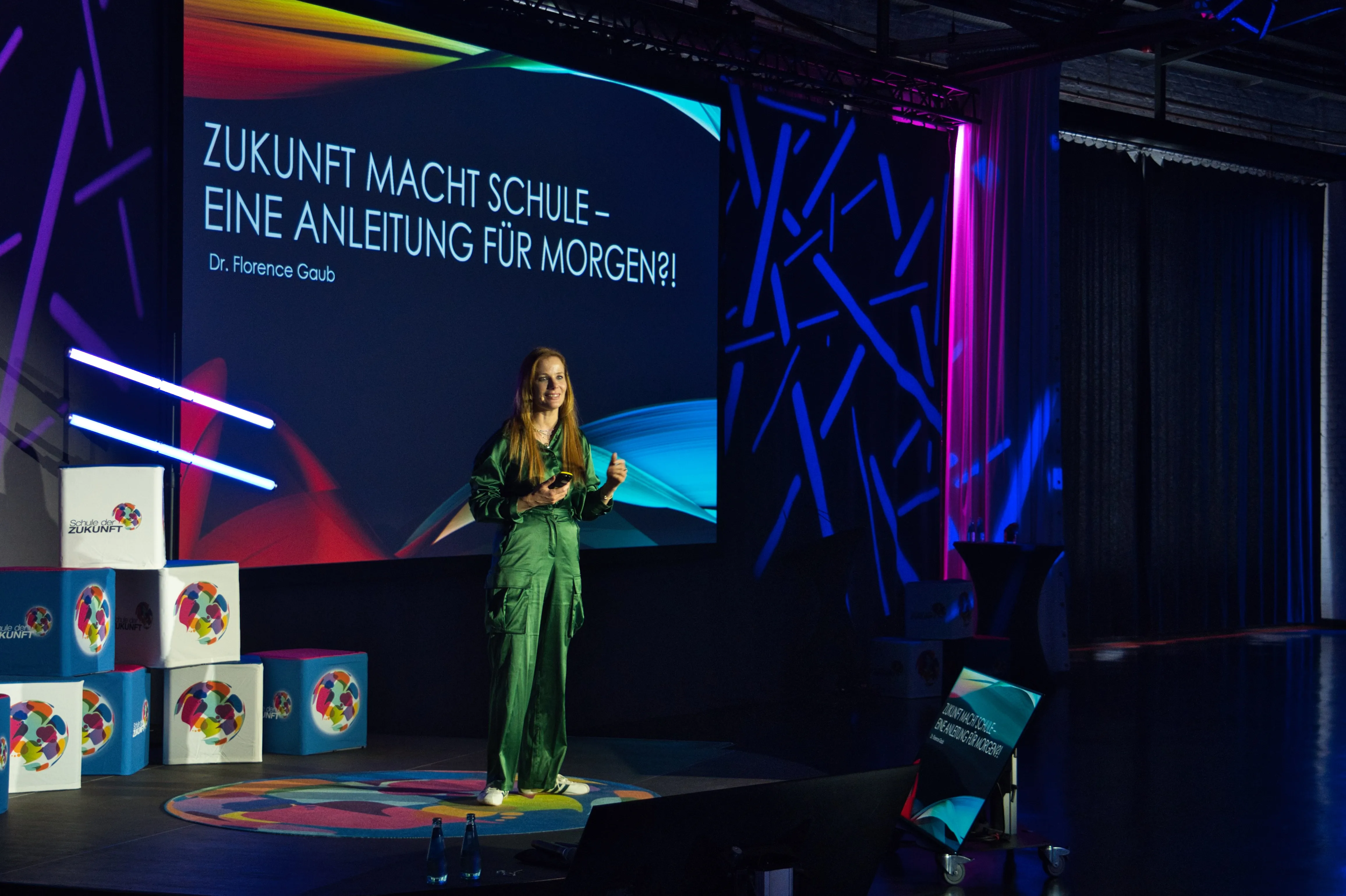 Speakerin steht auf der Bühne mit Präsentation im Hintergrund