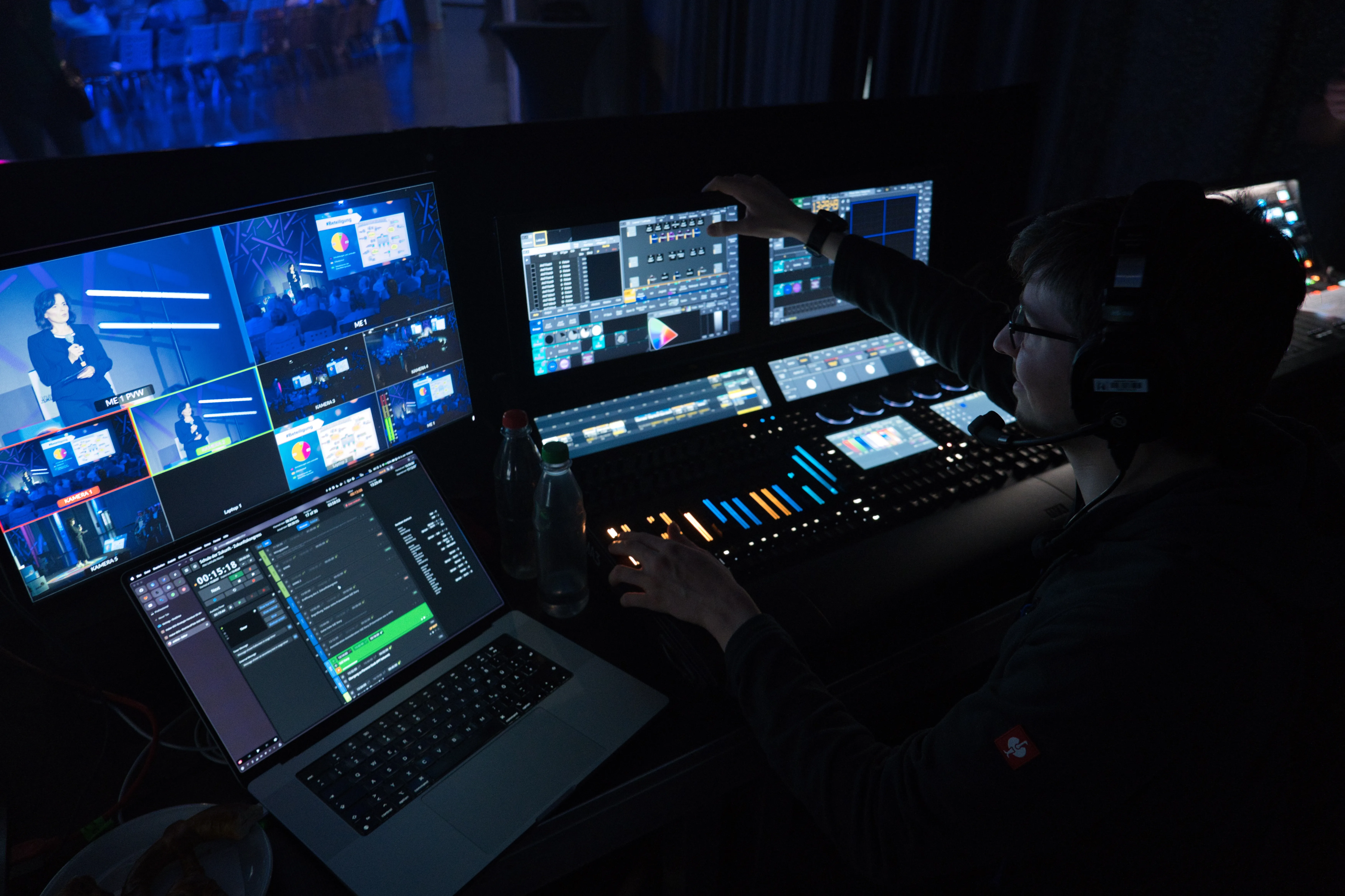 Person mit Lichtsteuerpult vor Bildschirmen